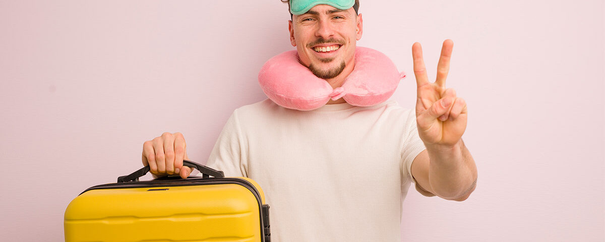 Η εικόνα δείχνει έναν κύριο να κρατάει μία κίτρινη βαλίτσα , να φοράει μία μάσκα ύπνου κι ένα μαξιλαράκι αυχένα