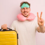 Η εικόνα δείχνει έναν κύριο να κρατάει μία κίτρινη βαλίτσα , να φοράει μία μάσκα ύπνου κι ένα μαξιλαράκι αυχένα