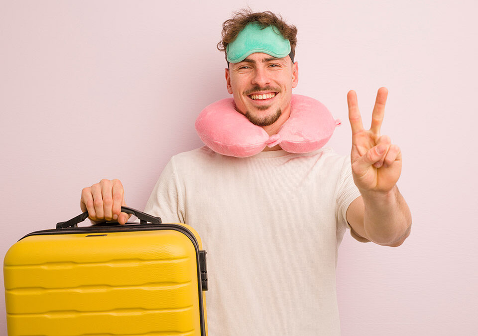 Η εικόνα δείχνει έναν κύριο να κρατάει μία κίτρινη βαλίτσα , να φοράει μία μάσκα ύπνου κι ένα μαξιλαράκι αυχένα