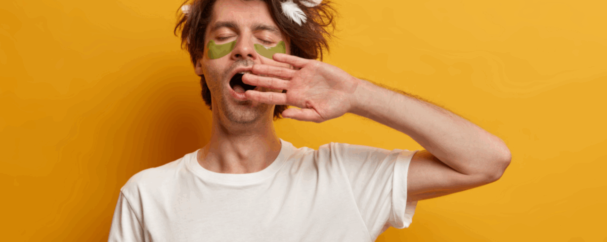 Ένας άντρας σε κίτρινο φόντο βάζει την παλάμη του μπροστά στο στόμα του και χασμουριέται.