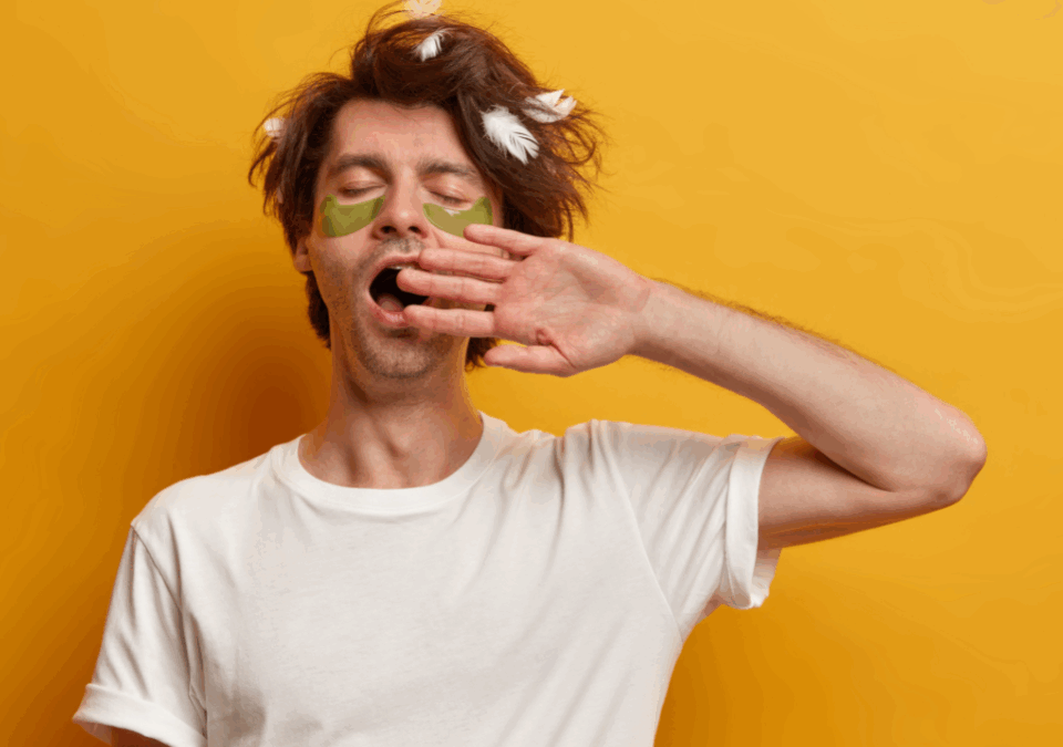 Ένας άντρας σε κίτρινο φόντο βάζει την παλάμη του μπροστά στο στόμα του και χασμουριέται.