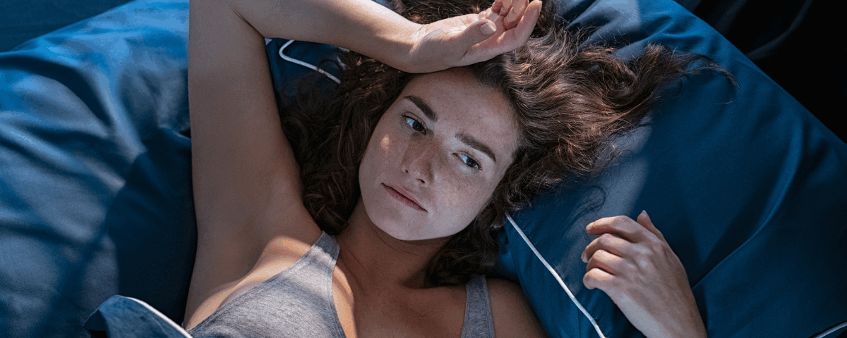 Μία γυναίκα που είναι ξαπλωμένη στο κρεβάτι και κρατάει το μέτωπό της προβληματισμένη.