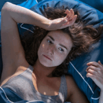 Μία γυναίκα που είναι ξαπλωμένη στο κρεβάτι και κρατάει το μέτωπό της προβληματισμένη.